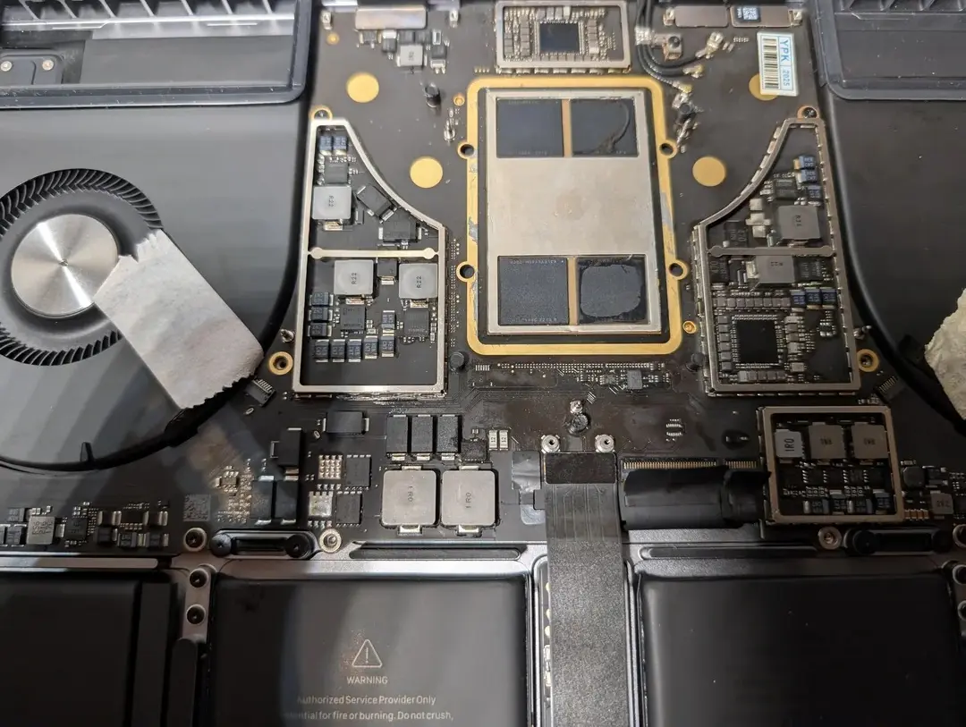 Damaged MacBook Pro logic board with visible burn hole near trackpad connector